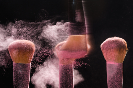 Make up, beauty and mineral cosmetic concept - brush brushing away pink powder from another over the black background.の写真素材