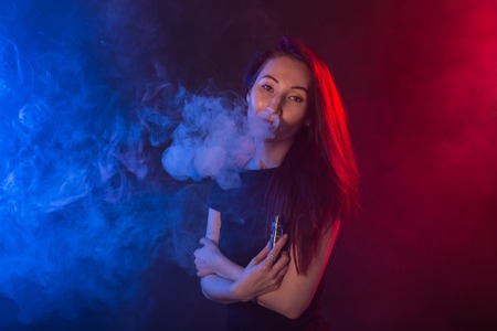 Portrait of girl in colored neon smoke with vape or electronic cigarette.の写真素材