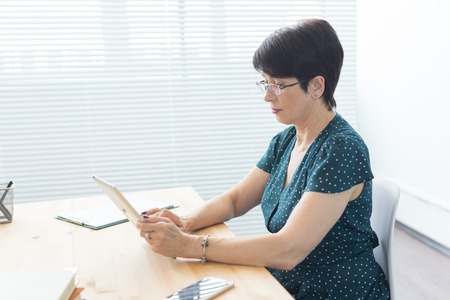 Business, technology and people concept - a serious woman sitting in office and use a tabletの写真素材