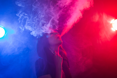 Young woman smoking vape or e-cigarette in neon lightの写真素材