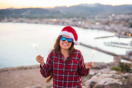 Christmas, holidays, people concept - woman in christmas hat and glasses holding sparklers over sea backgroundの写真素材