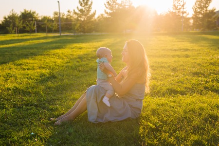 Young woman with boy on the meadow on a sunny day. Happy family on summer sunset. Mother with baby.の写真素材