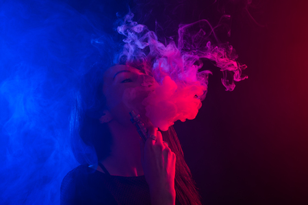 Young woman smoking vape or e-cigarette in neon lightの写真素材