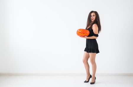 Portrait of a stylish brunette woman with halloween pumpkin over light background with copy spaceの写真素材