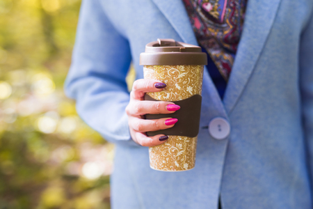 Close up of woman holding a cup of takeaway coffee cup on autumn streetの写真素材