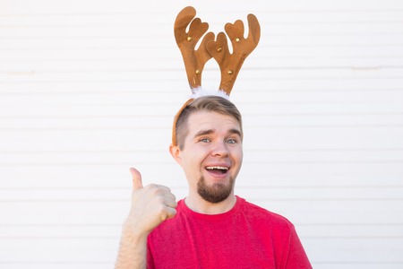 Holidays and christmas concept - Young man in deers horns with thumb up gesture on white background with copy spaceの写真素材