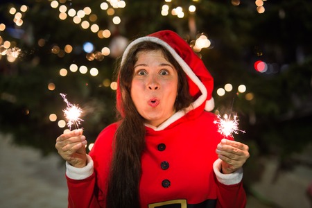 People, holidays and christmas concept - young woman in Santa costume with sparklers or Bengal light