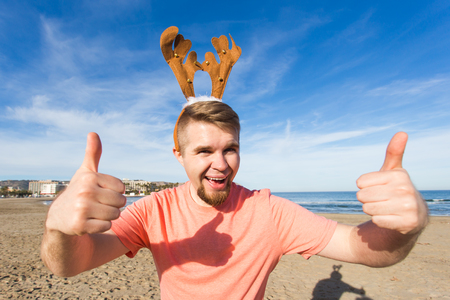 Holidays and Christmas concept - Man wearing rudolph horns with thumbs up at the beachの写真素材