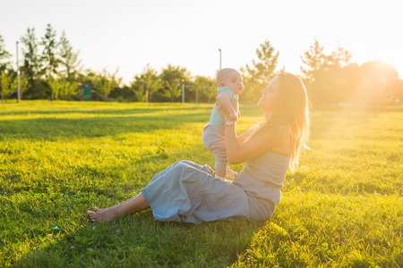 Young woman with boy on the meadow on a sunny day. Happy family on summer sunset. Mother with baby.の写真素材