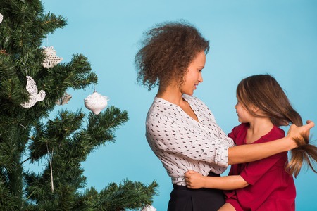 Mixed race mom and her daughter with Christmas tree on blue backgroundの写真素材