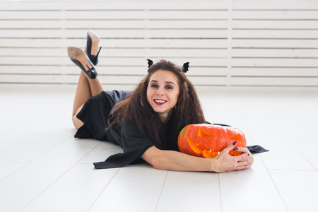 Happy gothic young woman in witch halloween costume smiling over white room backgroundの写真素材