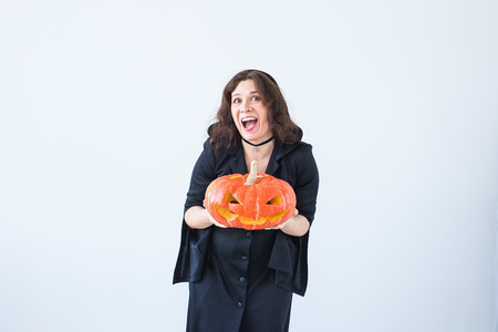 Excited happy young woman in halloween costume posing with carved pumpkin in lightroomの写真素材