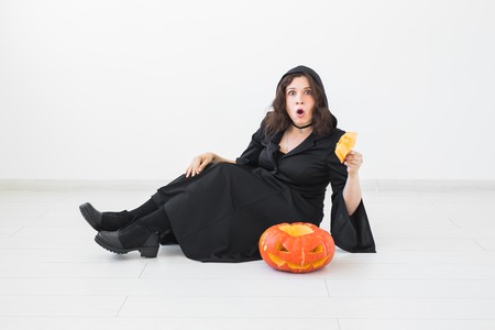 Surprised young woman in halloween costume posing with carved pumpkin in lightroomの写真素材