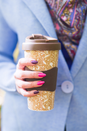 Close up of woman holding a cup of takeaway coffee cup on autumn streetの写真素材