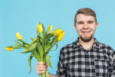Caucasian handsome man with bunch of yellow tulips on blue background.の写真素材