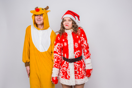 Holiday, Christmas and fun concept - Funny couple in deer costume and Santa Claus clothes are dancing on white backgroundの写真素材