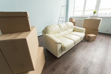 Relocation, moving and real estate concept- a new white sofa in empty room between an amount of boxesの写真素材
