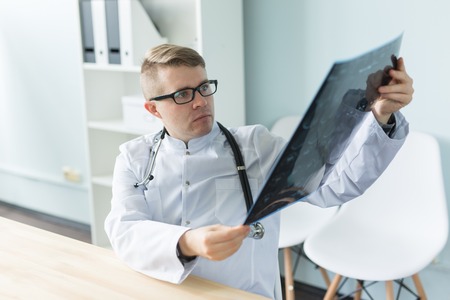 Healthcare, medical and people concept - handsome doctor sitting holding radiograph or tomography result in his handsの写真素材