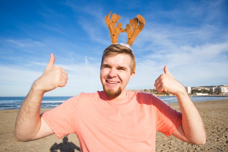 Holidays and Christmas concept - Man wearing rudolph horns with thumbs up at the beachの写真素材