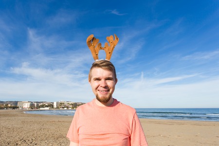 Fun, holidays and travel concept - Happy man in Christmas deer horns on the beachの写真素材