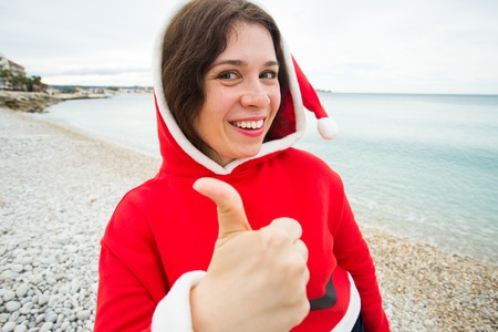 People, holidays and christmas concept - cheerful woman in santa hat making selfie and showing thumb upの写真素材