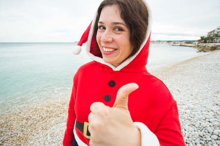 People, holidays and christmas concept - cheerful woman in santa hat making selfie and showing thumb upの写真素材