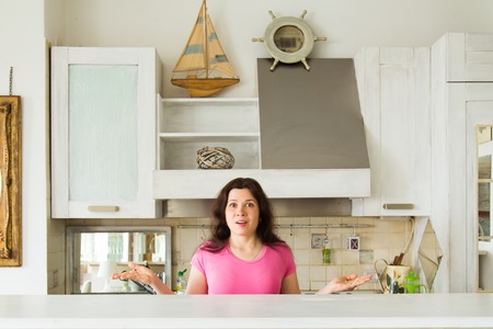 Housewives, emotions and people concept - Surprised young woman in the kitchen at homeの写真素材