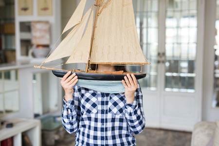 Hobby, interior and collecting concept - young woman holding the layout of a sailboat in the roomの写真素材