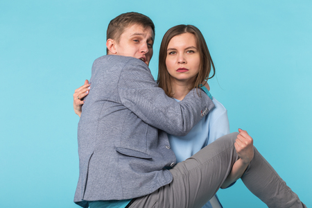 Family problems, responsibility, feminism and relationship concept - Woman carrying man in her arms on blue backgroundの写真素材