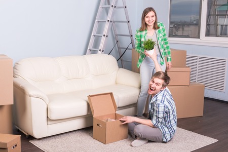Moving and real estate concept - happy couple having fun unpacking cardboard boxes at new homeの写真素材