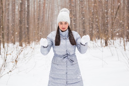 Winter, season and people concept - Woman in grey coat and white hat walking in winter park and playing with snowの写真素材