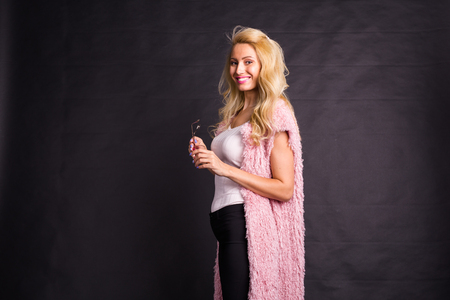 Fashion and beauty concept - portrait of blond model in pink cardigan posing over dark background with copy spaceの写真素材