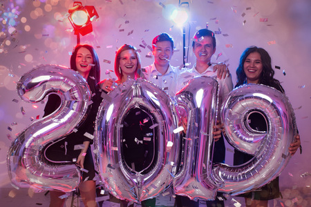 New 2019 Year is coming. Group of cheerful young people holding silver colored numbers and throwing confetti on the party.の写真素材
