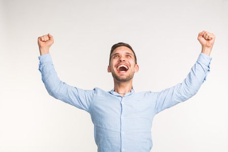 Emotions, victory and people concept - Handsome joyful man with his arms up over white background