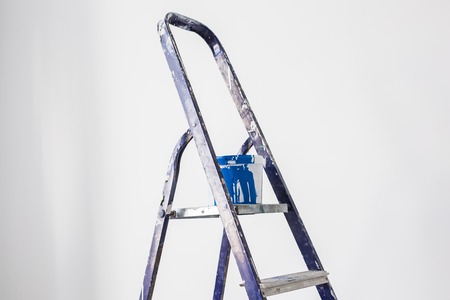 Renovation, redecoration and repair concept - Ladder with a container of blue paint over white wall