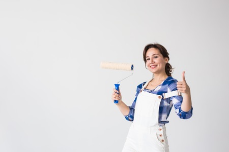 Repair, renovation, new home and people concept - young woman doing redecoration and show us thumbs up over white wall with copy spaceの写真素材