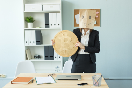 Crypto currency, money, blockchain concept - funny woman with package on her head show us a huge bitcoin. She looks like crazyの写真素材