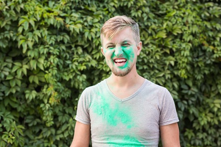 Holiday, holi and people concept - Smiling man posing with green powder on his shirt and face.の写真素材