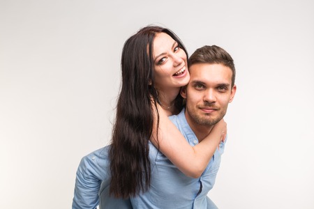 Young male carrying his girlfriend piggyback against a white backgroundの写真素材