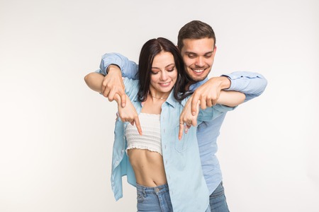 People and gesture concept - young pretty woman and handsome man pointing down over white backgroundの写真素材