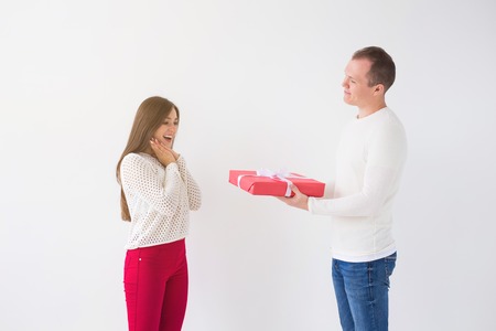 People, christmas, birthday, holidays and valentines day concept - Handsome man is giving his girlfriend a gift box on white backgroundの写真素材