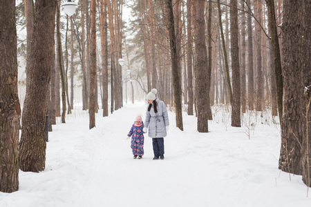 Winter, childhood and people concept - mother is walking with her little daughter in snowy forestの写真素材