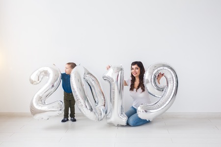 New year, celebration and holidays concept - mother and son sitting near sign 2019 made of silver balloons for new year in white room backgroundの写真素材