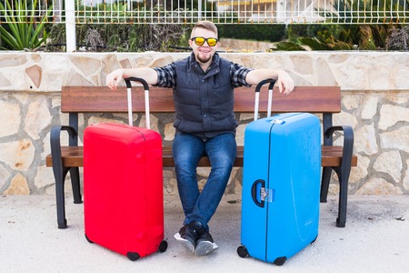 Travel, tourism and people concept - happy man sitting on a bench with two suitcases, he is ready for travellingの写真素材