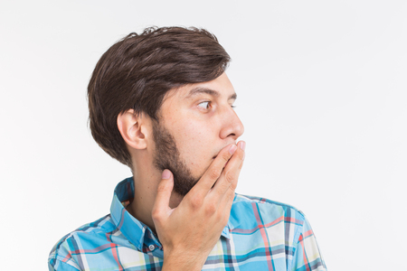 People, emotions and gesture concept - young surprised man covering his mouth with his hand on white backgroundの写真素材