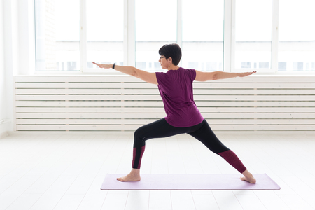 People, sport and healthcare concept - Middle-aged woman practicing yoga, standing in Warrior two exerciseの写真素材