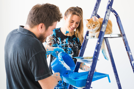 Pet, redecoration and relationship concept - Young funny couple with cat doing renovation in new apartmentの写真素材
