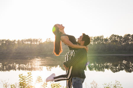 Romantic, love and people concept - Man holding woman in his arms on the beach of the river on a sunsetの写真素材