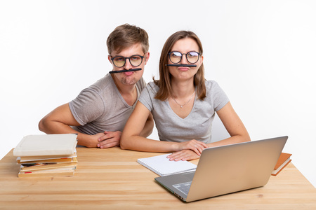 Education and people concept - a couple of young students in glasses look like they are bored of learning homework and make a stupid jokesの写真素材
