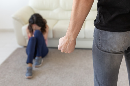 Victim, domestic violence and abuse concept - man threatening with fist to crying woman on floor scared and terrified in domestic violenceの写真素材